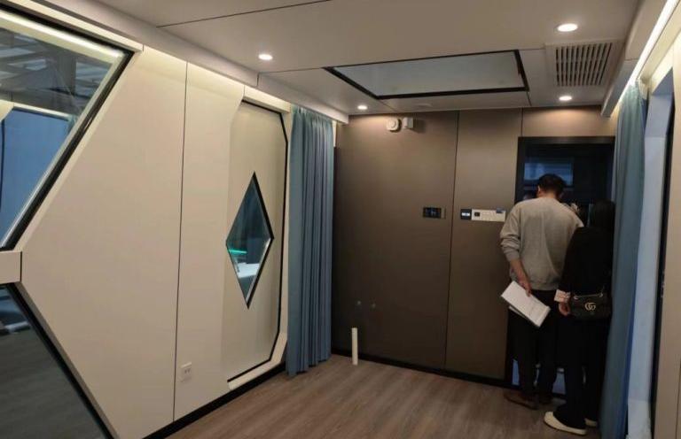 Вид изнутри LUBAN CABIN C30 с уникальным ромбовидным окном, синими шторами и темными стеновыми панелями.