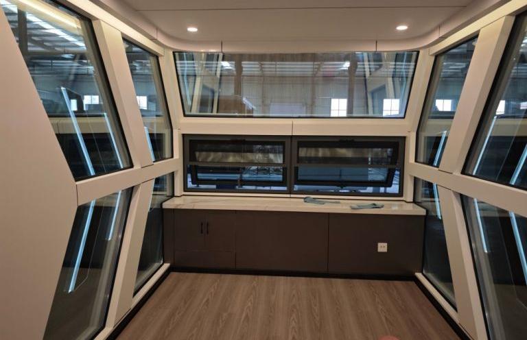 Interior of LUBAN CABIN C30 featuring angular windows, kitchenette with dark cabinets, and wooden flooring.